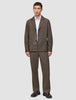 En mand iført en mørkbeige overshirt fra Atelier, en hvid skjorte med knapper, matchende bukser og mørke læderloafers.