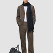 En mand iført en brun Atelier Overshirt Dark Beige, en hvid skjorte og et sort tørklæde står ved siden af en sort læderrejsetaske.