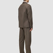 En person set bagfra, iført en Atelier Overshirt i mørk beige med matchende bukser og mørke loafers.