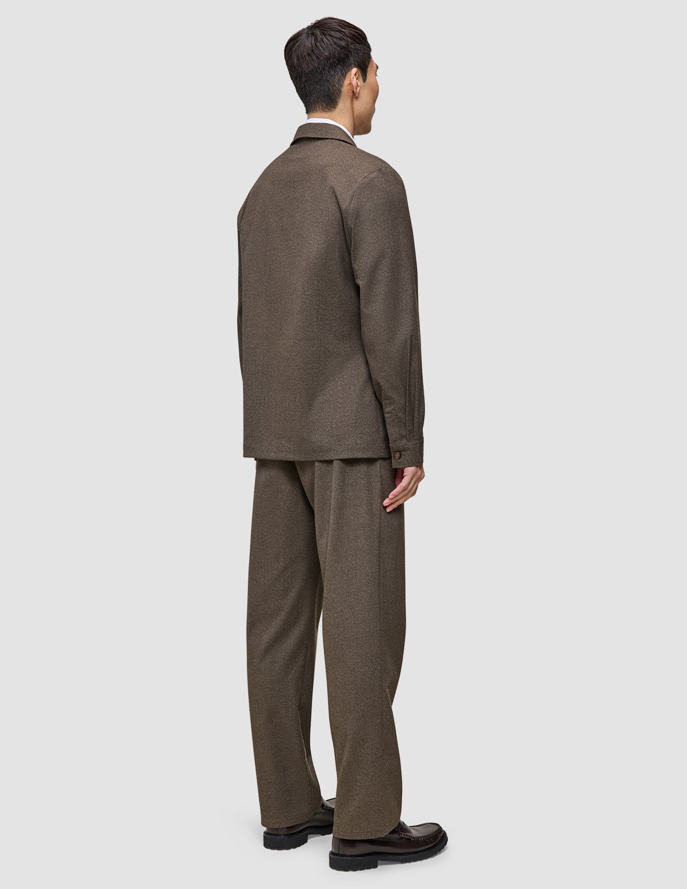 En person set bagfra, iført en Atelier Overshirt i mørk beige med matchende bukser og mørke loafers.
