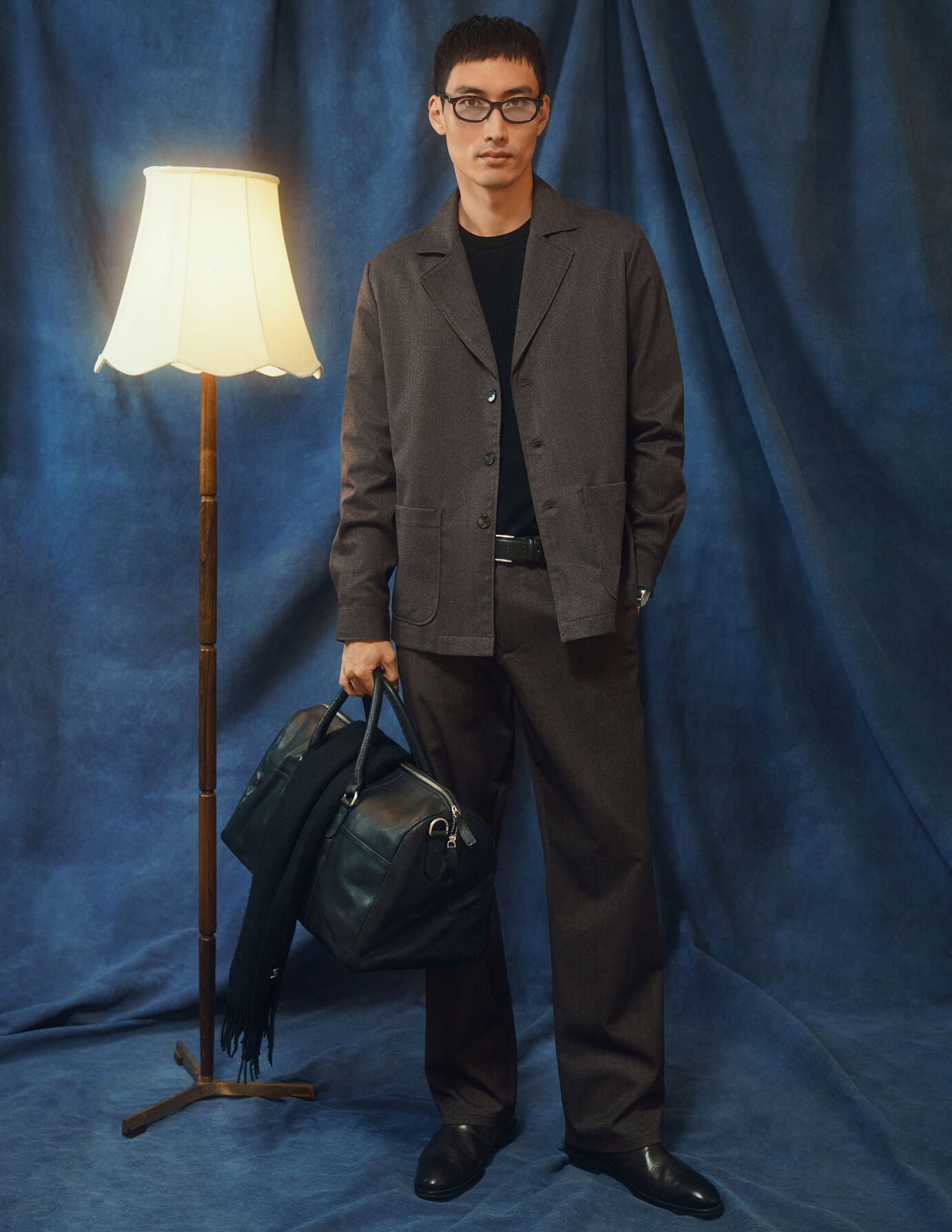 En mand iført en mørkbeige overshirt fra Atelier, matchende bukser og en sort T-shirt holder en lædertaske i blazerstil.