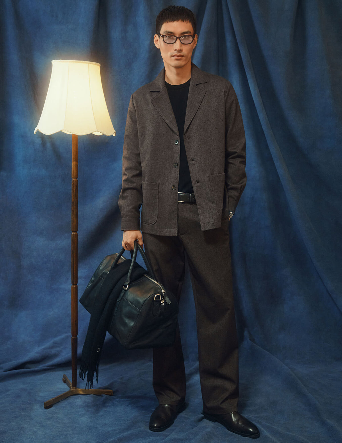 En mand iført en mørkbeige overshirt fra Atelier, matchende bukser og en sort T-shirt holder en lædertaske i blazerstil.