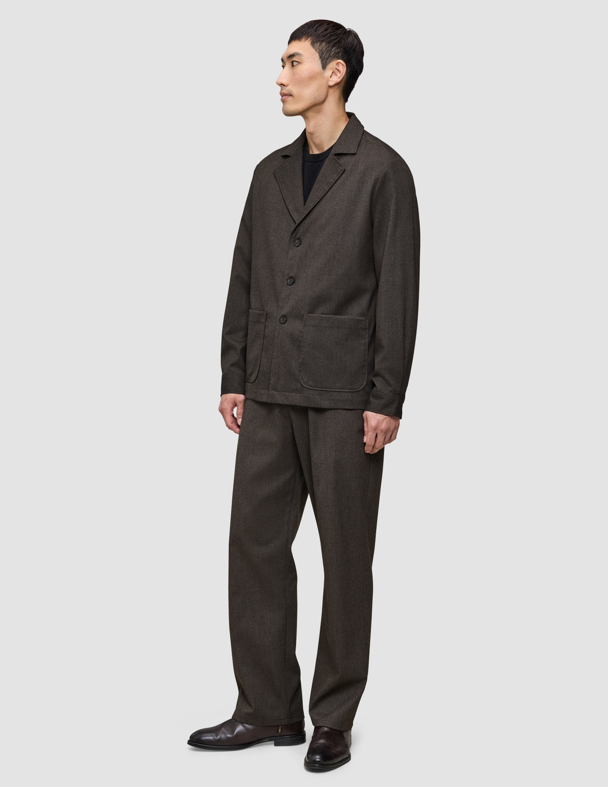 En mand iført en Atelier Overshirt i mørkebrun i et elegant dansk design med matchende bukser.
