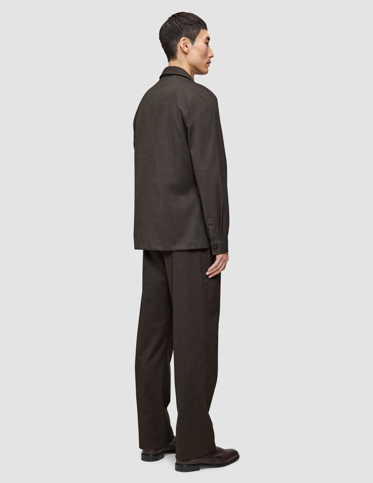 En person set fra siden, iført en mørkebrun Atelier Overshirt og matchende bukser i et rent, dansk design.