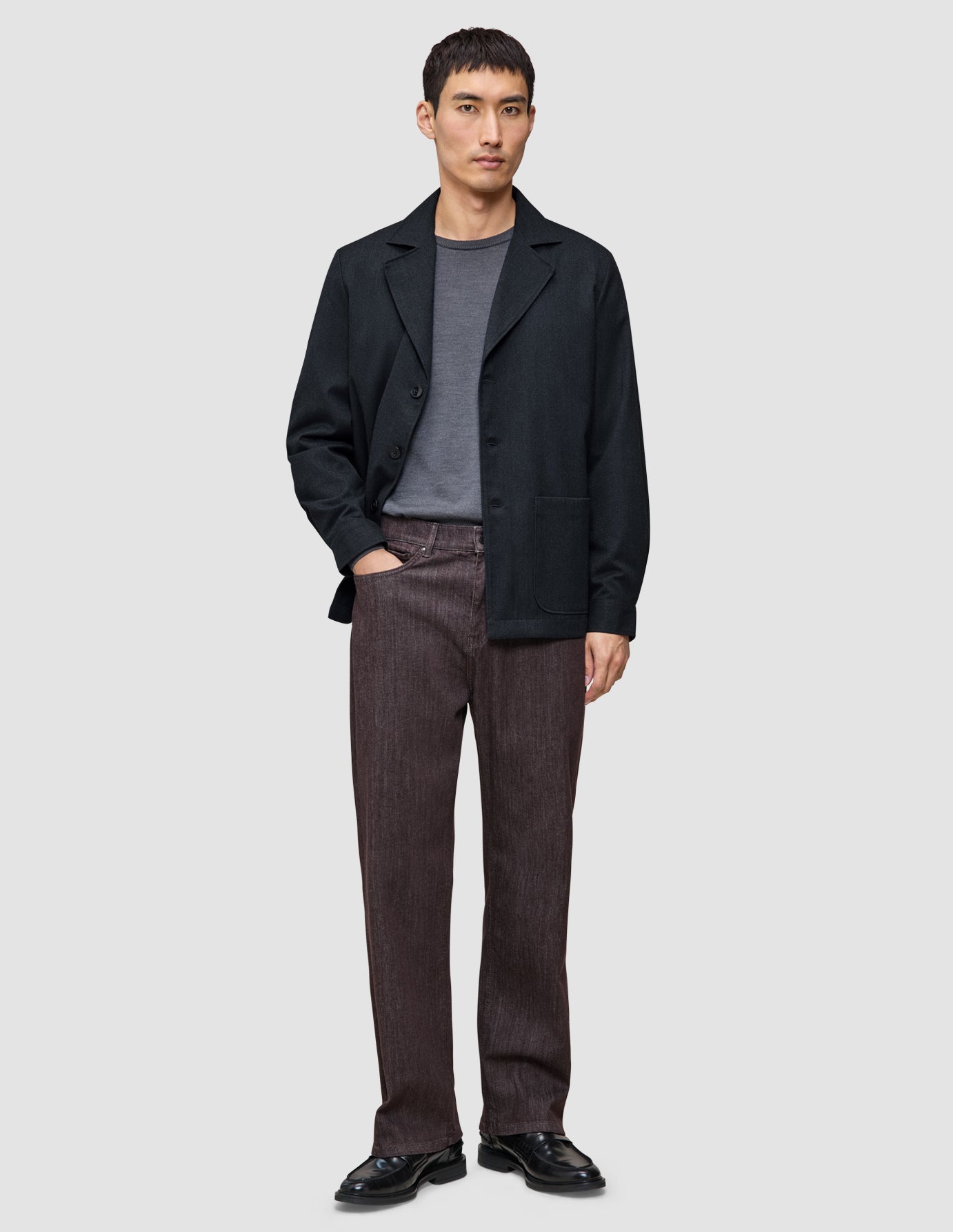 En mand iført en mørkeblå Atelier-overshirt, en grå T-shirt, brune Atelier-bukser og sorte lædersko.