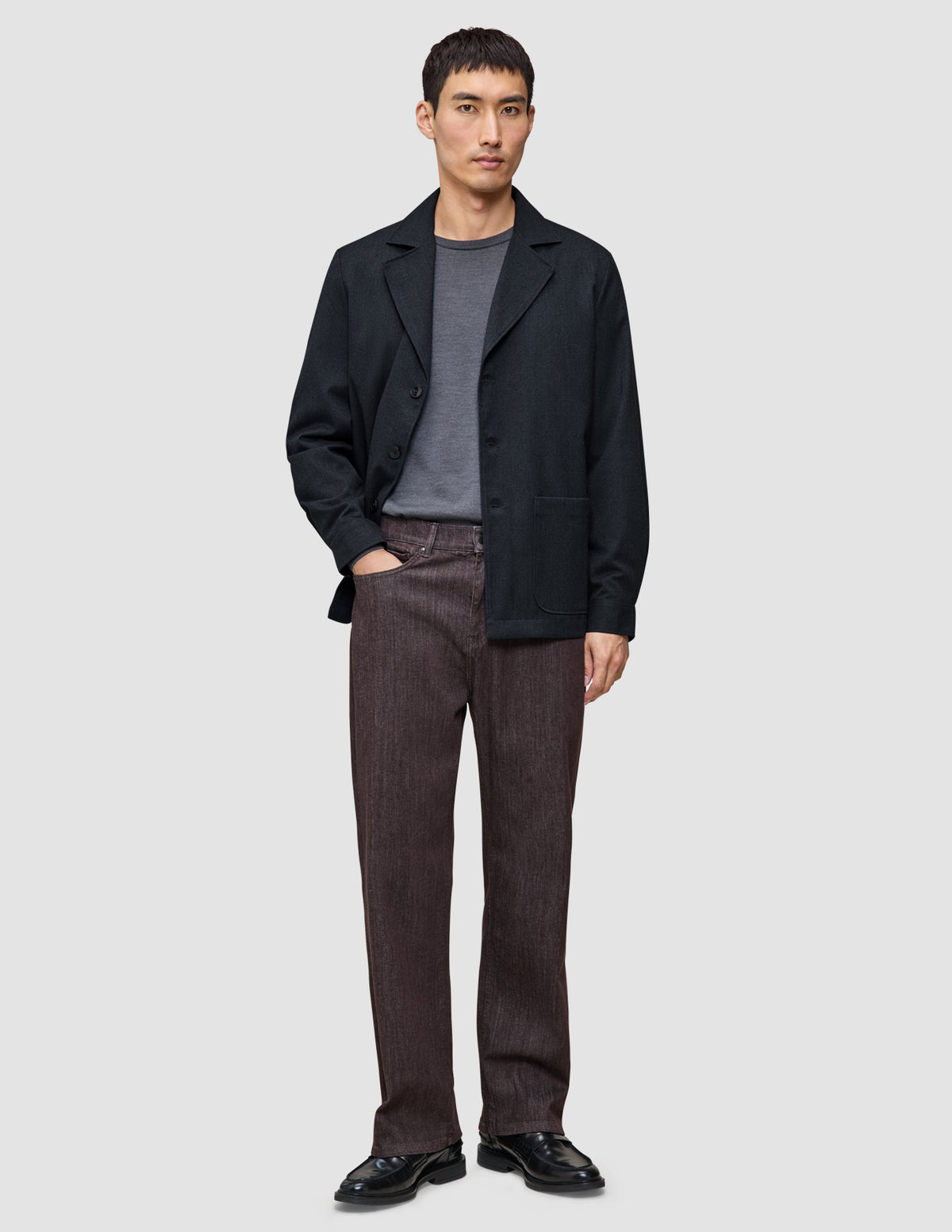 En mand iført en mørkeblå Atelier-overshirt, en grå T-shirt, brune Atelier-bukser og sorte lædersko.