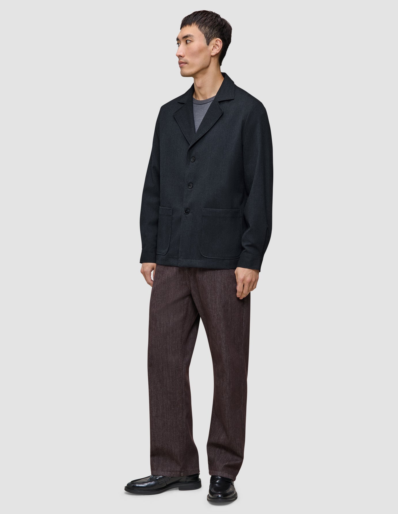 En mand iført en mørk marineblå Atelier Overshirt, en grå T-shirt, brune bukser og sorte loafers.