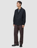 En mand iført en mørk marineblå Atelier Overshirt, en grå T-shirt, brune bukser og sorte loafers.