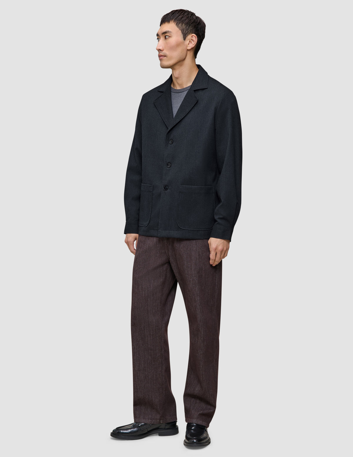 En mand iført en mørk marineblå Atelier Overshirt, en grå T-shirt, brune bukser og sorte loafers.