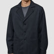 En mand bærer en Atelier Overshirt i mørk marineblå med en krave med udskæring, to påsatte lommer foran og en pasform i blazerstil.
