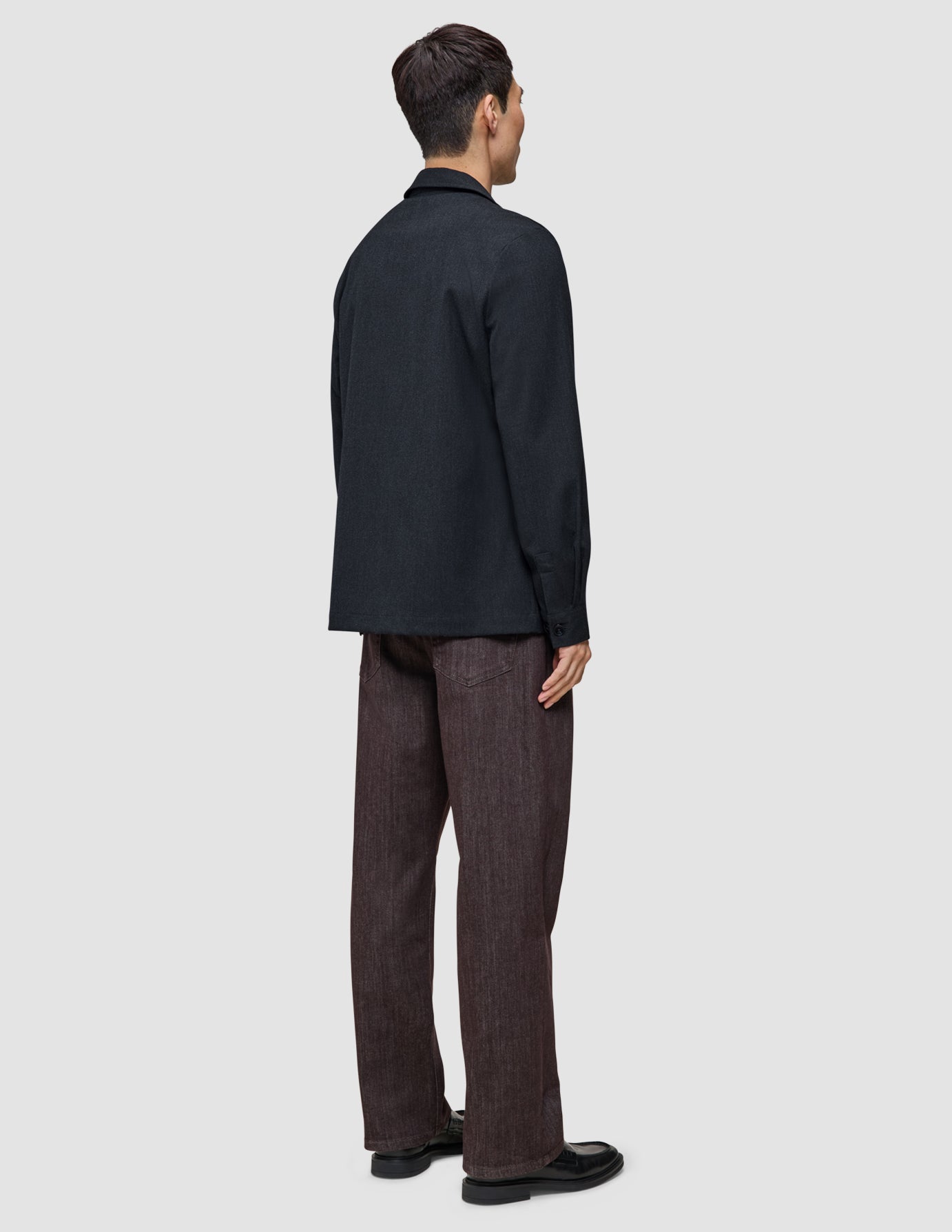 En person set bagfra, iført en Atelier Overshirt i mørk marineblå over bukser og sorte loafers.