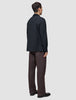 En person set bagfra, iført en Atelier Overshirt i mørk marineblå over bukser og sorte loafers.