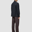 En person set bagfra, iført en Atelier Overshirt i mørk marineblå over bukser og sorte loafers.