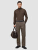 En mand iført en brun sweater med kvartlængde lynlås og et par Atelier Pants Relaxed i mørk beige, der holder en mørk taske.