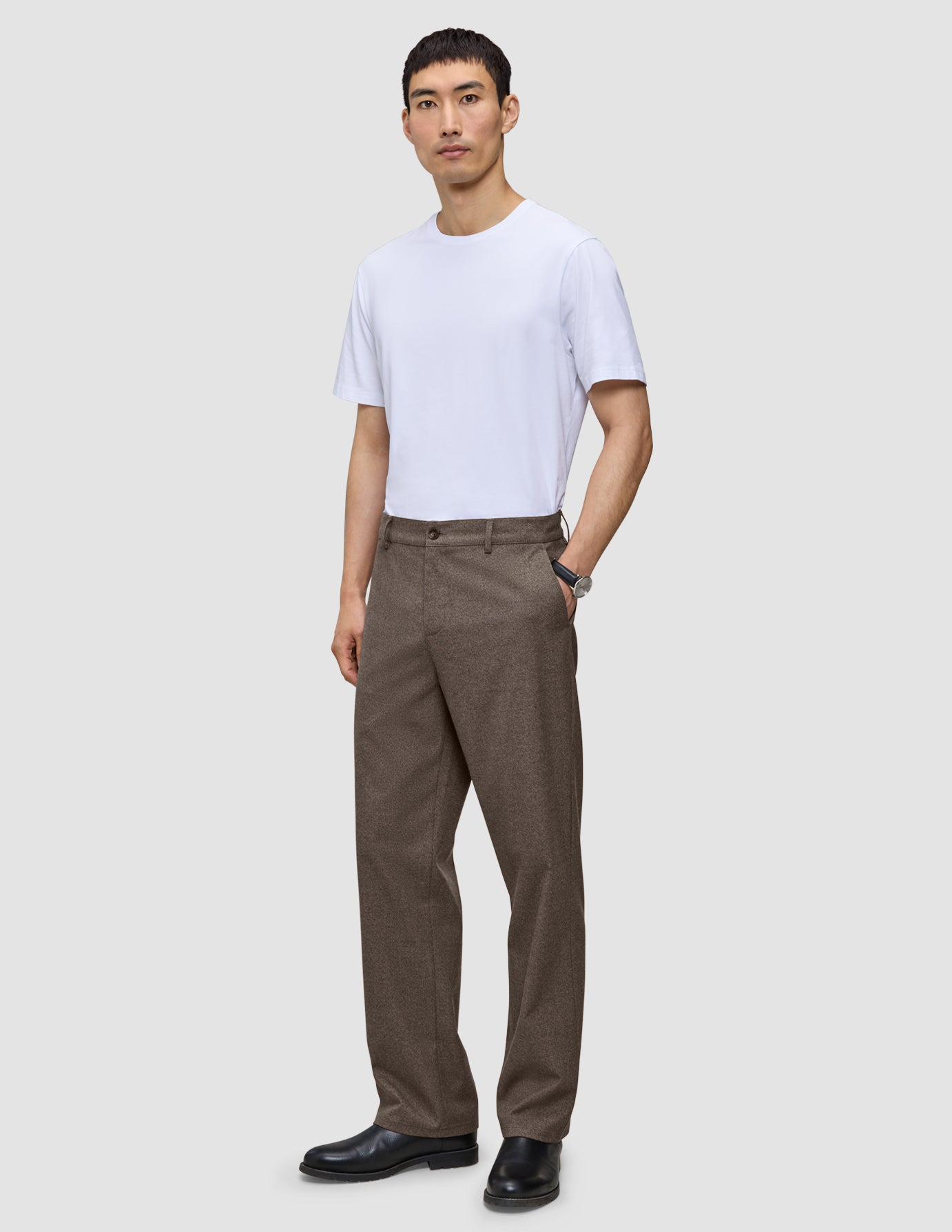 En mand har en hvid T-shirt, sorte sko og et par Atelier Pants Relaxed Dark Beige i kraftigt, brudt twill på.