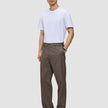 En mand har en hvid T-shirt, sorte sko og et par Atelier Pants Relaxed Dark Beige i kraftigt, brudt twill på.