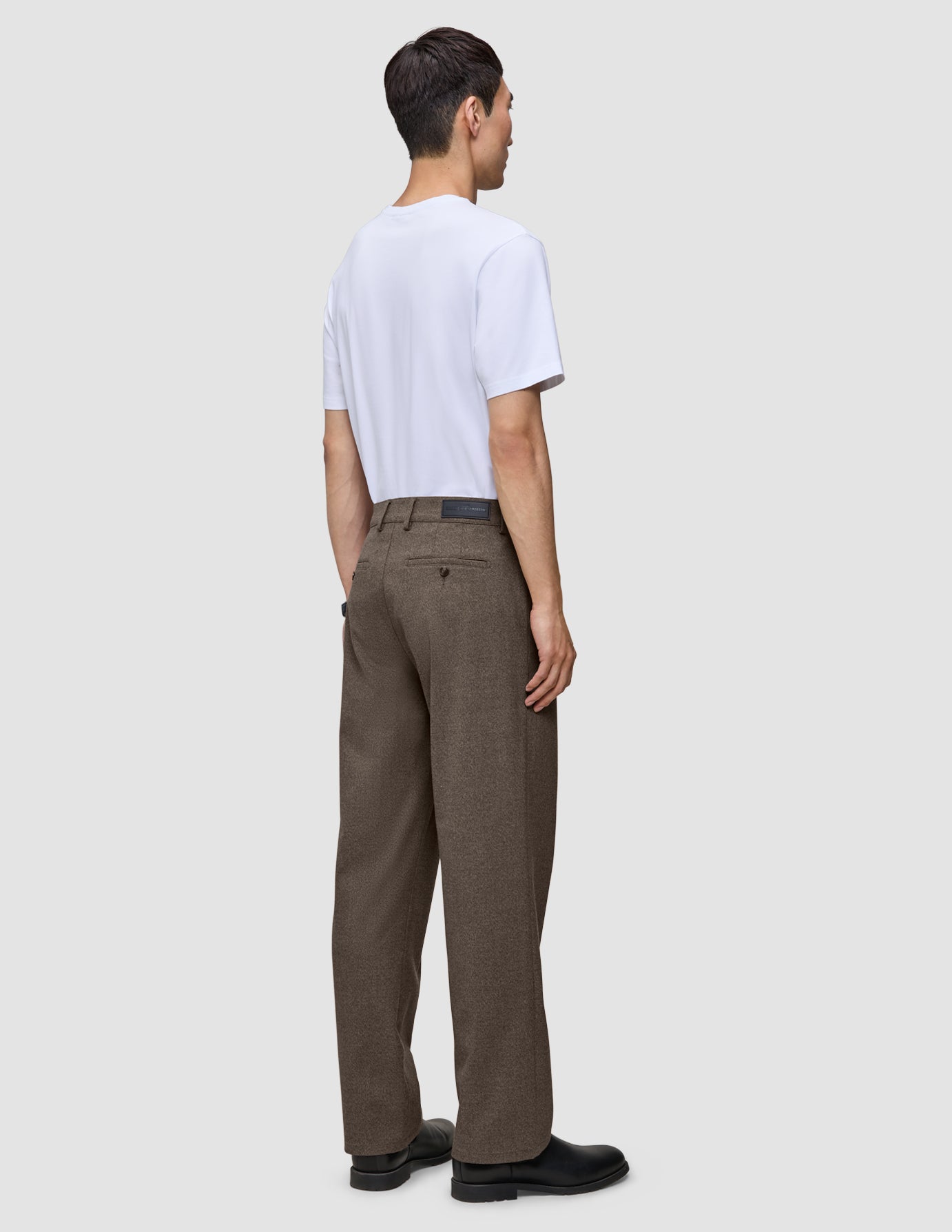 En person set bagfra, iført en hvid T-shirt og Atelier Pants Relaxed Dark Beige i kraftig, brudt twill.