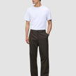En mand i en hvid T-shirt og mørkebrune Atelier Pants Relaxed, kombineret med mørke lædersko for at skabe et afslappet, skræddersyet look.
