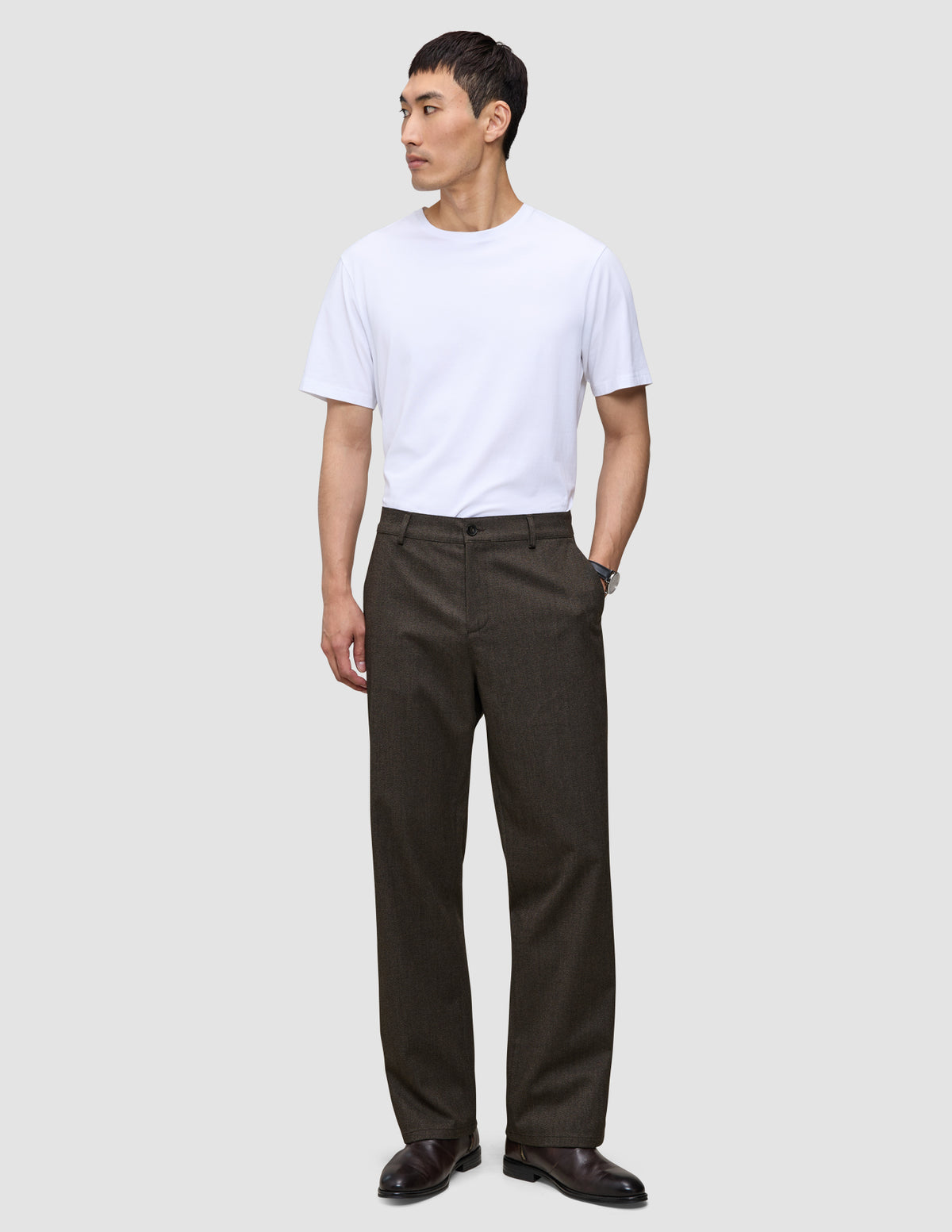 En mand i en hvid T-shirt og mørkebrune Atelier Pants Relaxed, kombineret med mørke lædersko for at skabe et afslappet, skræddersyet look.