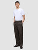 En mand har en hvid T-shirt på og et par Atelier Pants Relaxed i mørkebrun, syet i et afslappet-siddende brudt twill-stof.