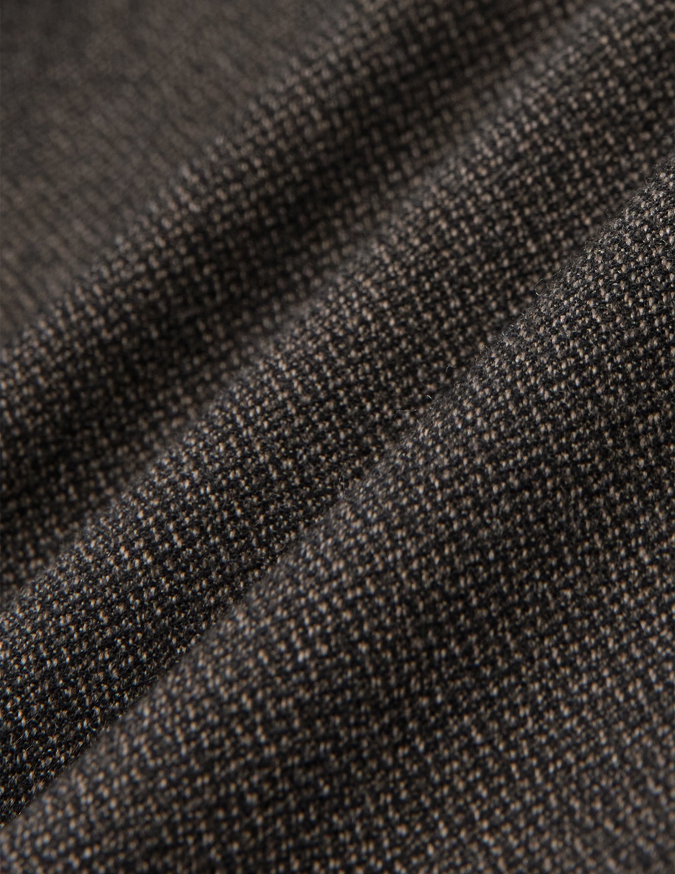 Nærbillede af de opfoldede Atelier Pants Relaxed i mørkebrun, brudt twill-stof med et struktureret, plettet væv.