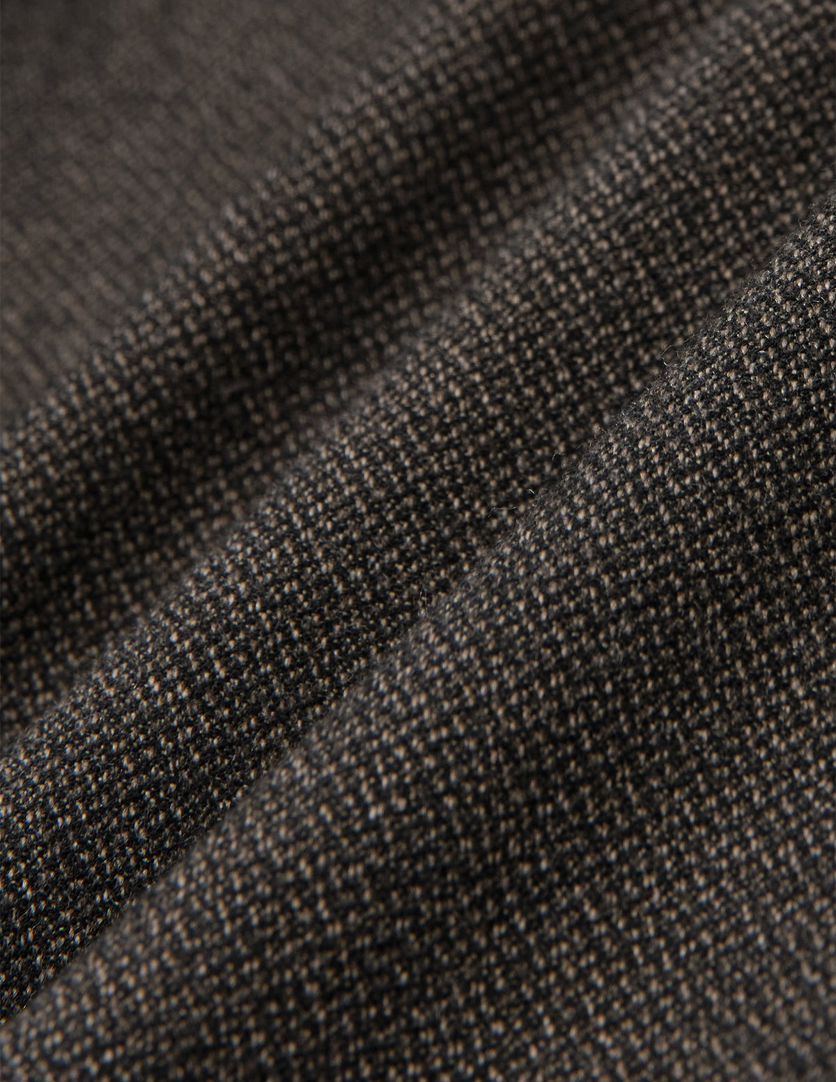 Nærbillede af de opfoldede Atelier Pants Relaxed i mørkebrun, brudt twill-stof med et struktureret, plettet væv.