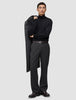 En person iført en sort rullekravebluse og et par mørkegrå Atelier Pants Relaxed med en frakke hængende over skulderen.