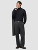 En mand i en sort rullekravebluse og mørkegrå Atelier Pants Relaxed, der har en frakke over skulderen.