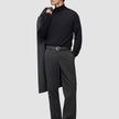 En mand i en sort rullekravebluse og mørkegrå Atelier Pants Relaxed, der har en frakke over skulderen.