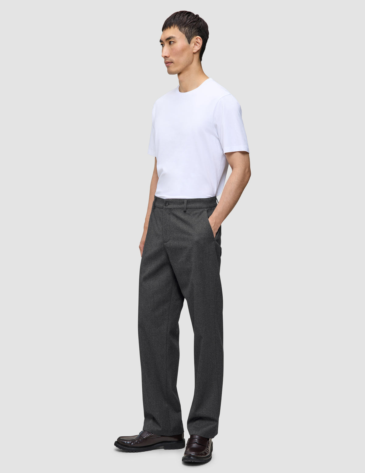 En mand iført en hvid T-shirt og et par Atelier Pants Relaxed i mørkegrå, med afslappet pasform og i et brudt twill-stof.