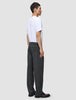 En mand i en hvid T-shirt, iført Atelier Pants Relaxed i mørkegrå og mørke loafers.