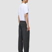 En mand i en hvid T-shirt, iført Atelier Pants Relaxed i mørkegrå og mørke loafers.