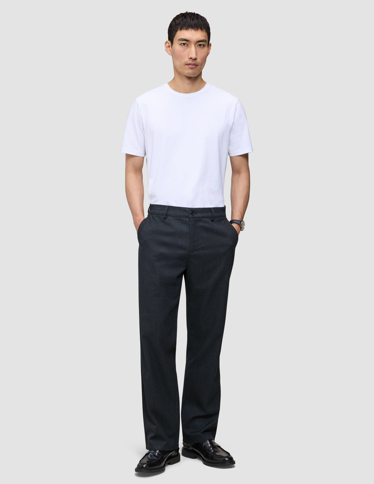 En mand i en hvid T-shirt, sorte loafers og Atelier Pants Relaxed Dark Navy, der er indbegrebet af afslappet dansk design.
