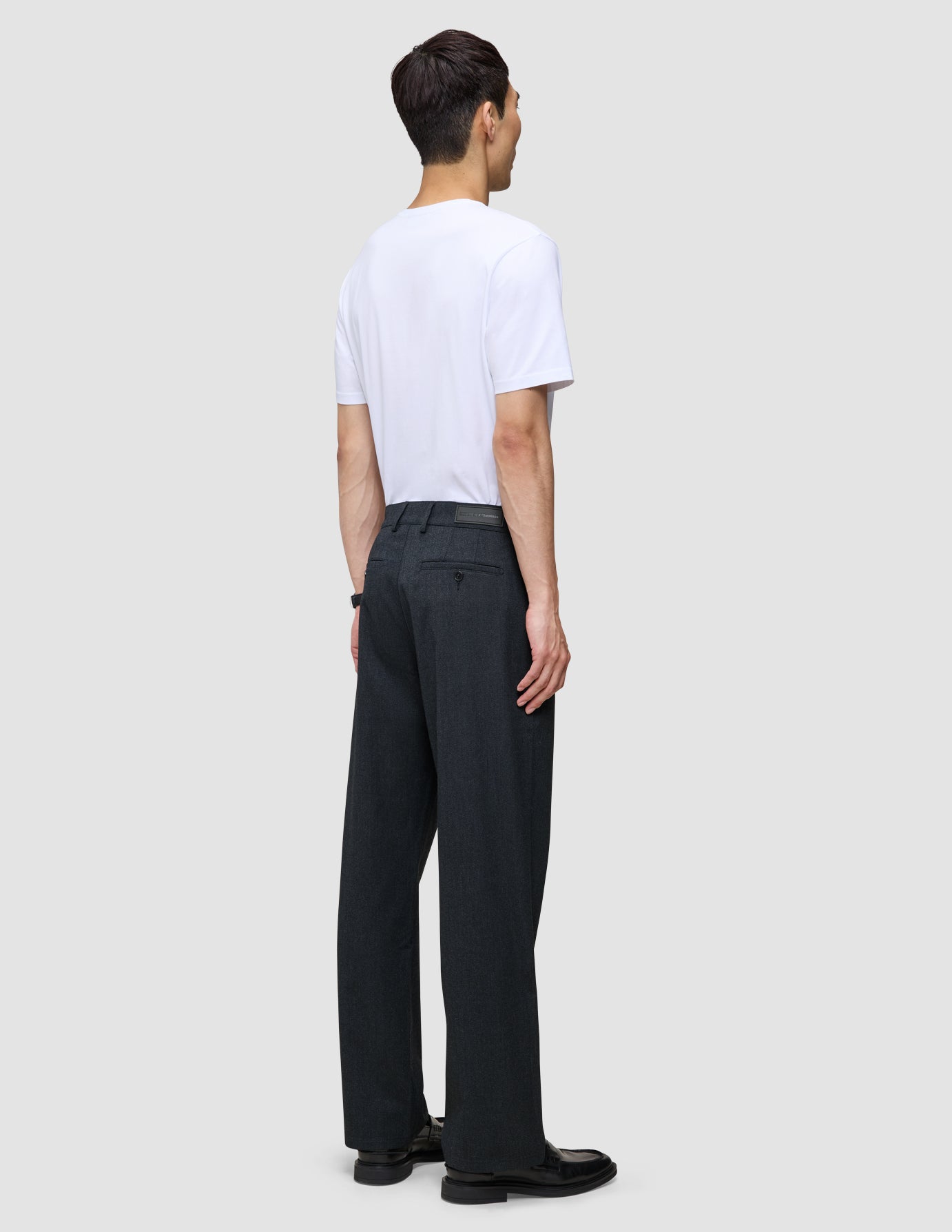 En mand set bagfra, iført en hvid T-shirt og et par Atelier Pants Relaxed i mørk marineblå.
