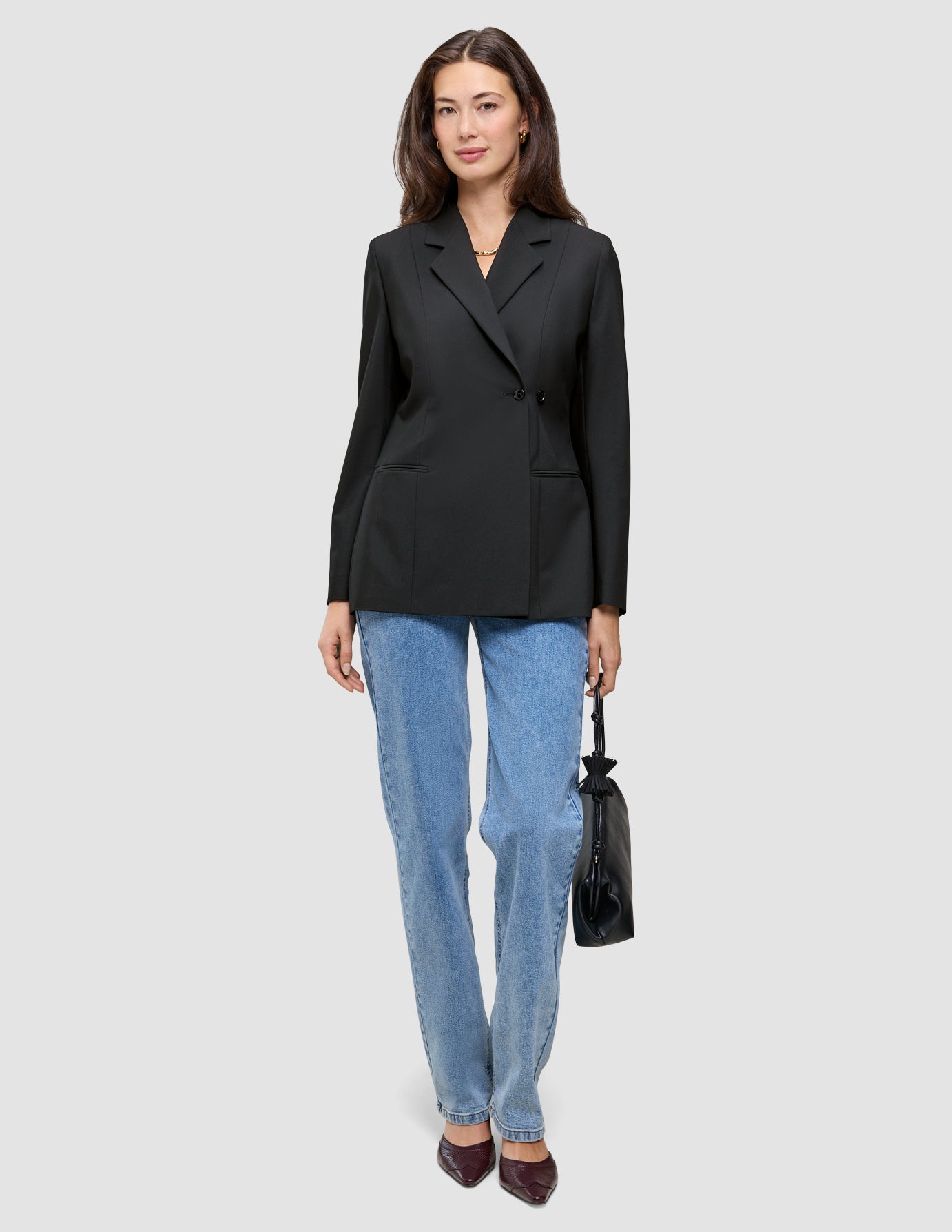 En kvinde iført en sort Avira-blazer til kvinder og blå jeans, der holder en lille sort håndtaske.