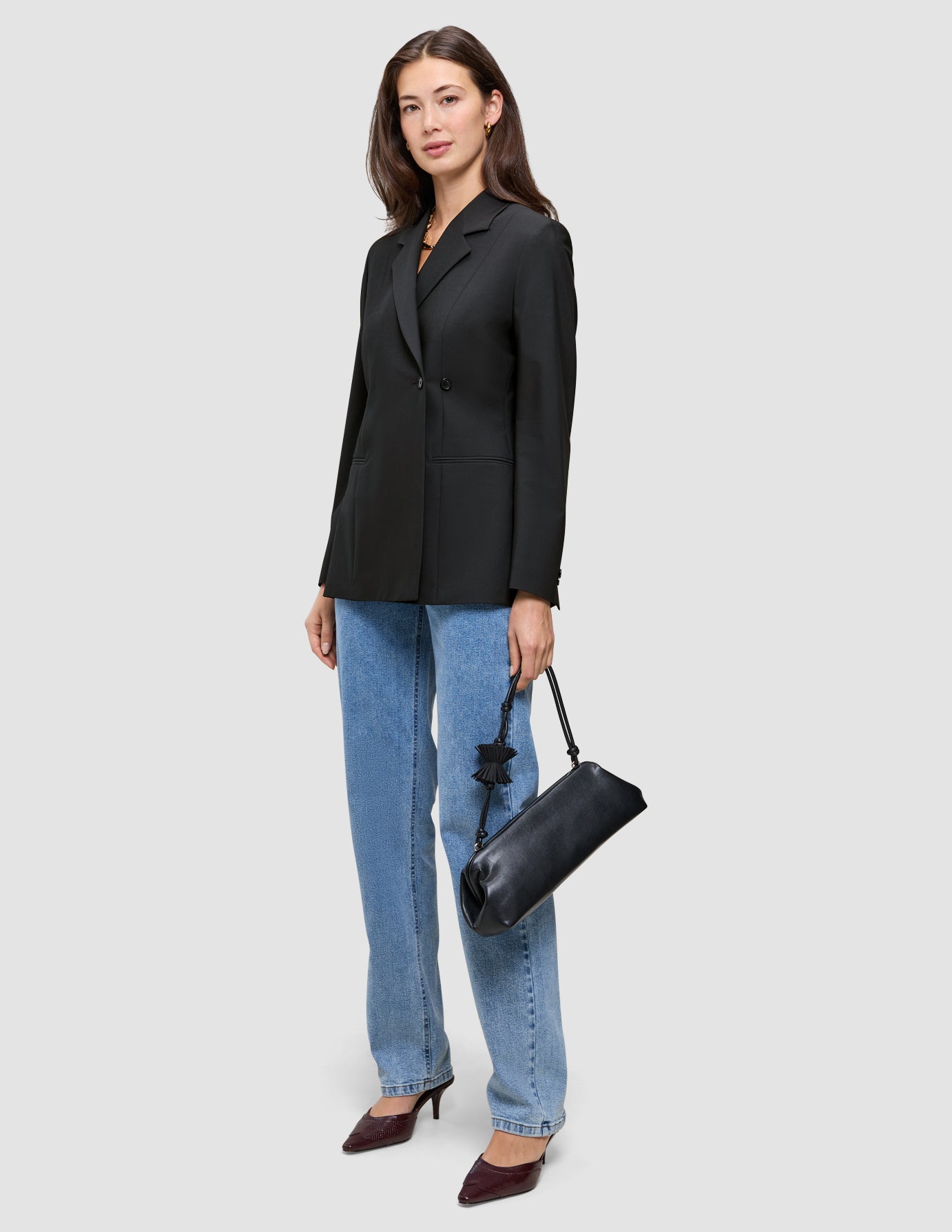 En kvinde er klædt i en sort Avira-blazer til kvinder, blå jeans og mørke højhælede sko og bærer en sort skuldertaske.
