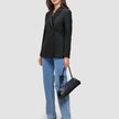 En kvinde er klædt i en sort Avira-blazer til kvinder, blå jeans og mørke højhælede sko og bærer en sort skuldertaske.