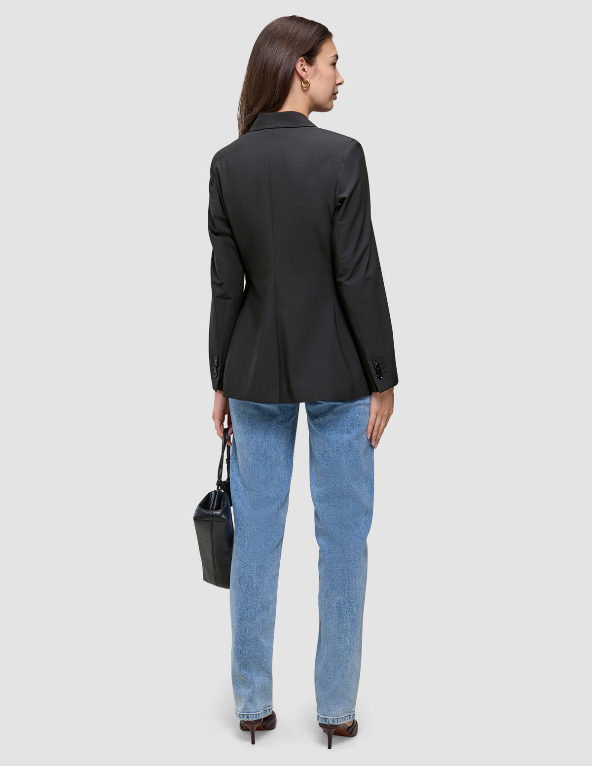Bagfra-billede af en kvinde iført en sort Avira-blazer til kvinder, lysblå jeans og mørke højhælede sko, der holder en sort håndtaske.