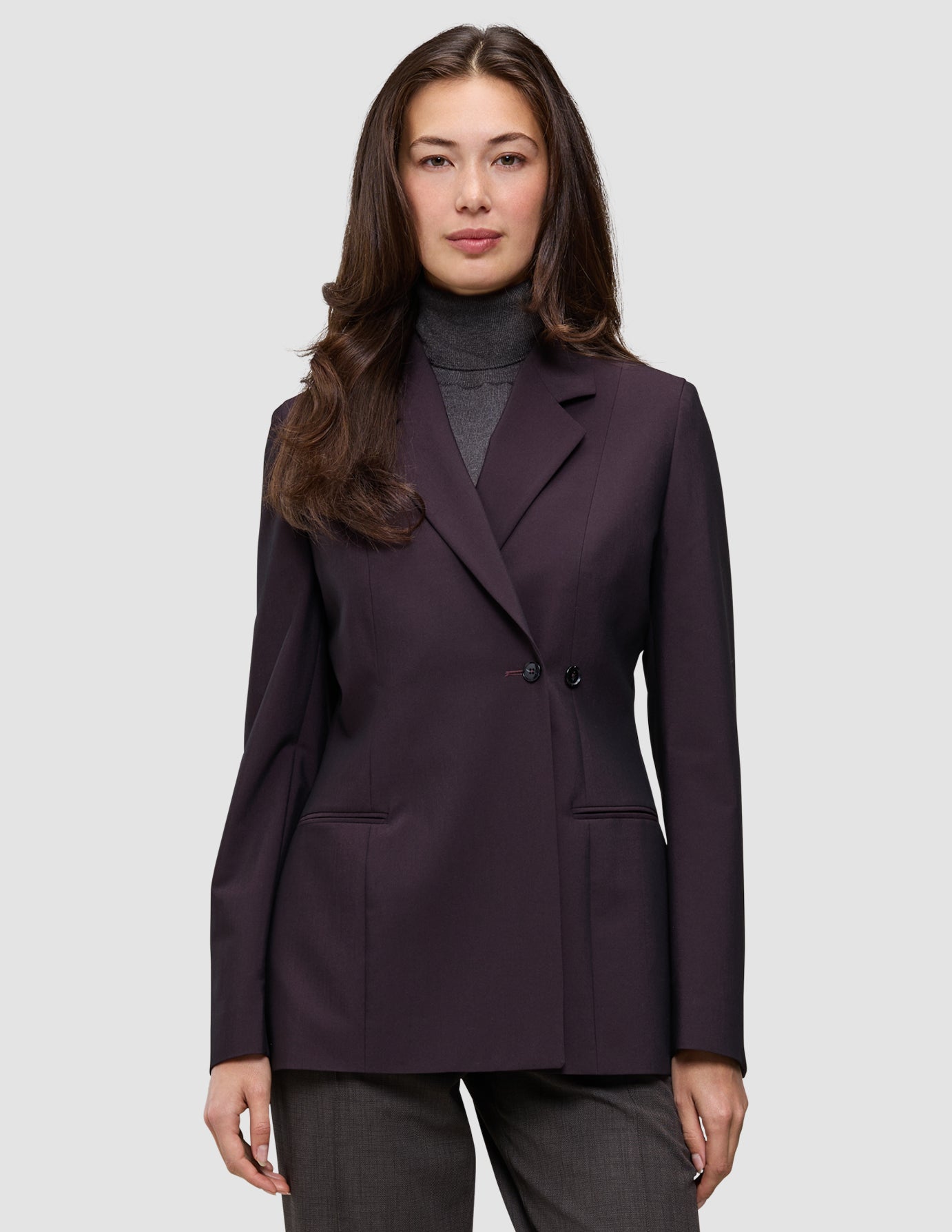 En kvinde iført en dobbeltradet Women’s Avira Blazer i farven Burgundy Berry over en grå rullekravebluse.