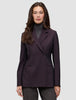 En kvinde iført en dobbeltradet Women’s Avira Blazer i farven Burgundy Berry over en grå rullekravebluse.