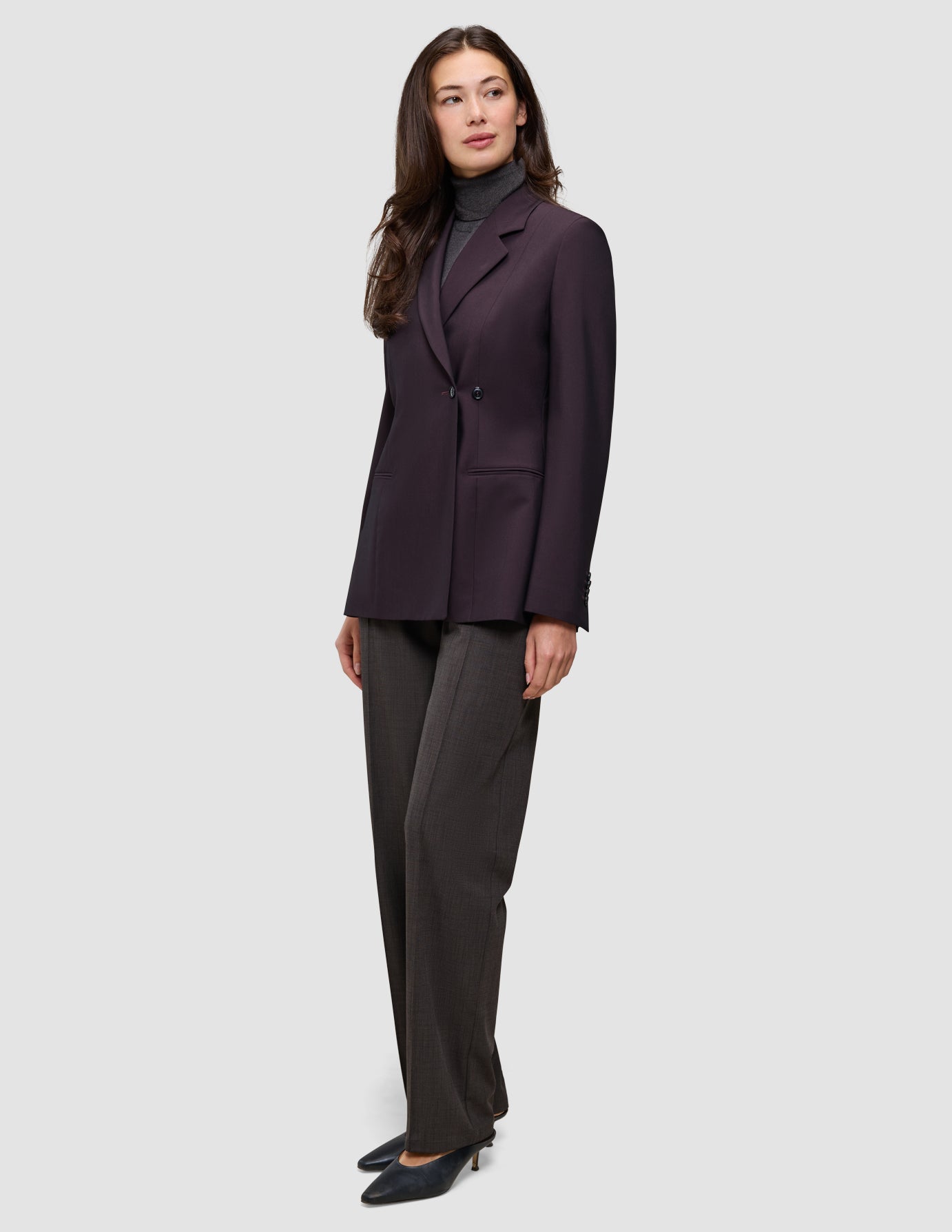 En kvinde iført en Avira-blazer i farven Burgundy Berry over en grå rullekravebluse og mørke bukser i dansk stil.