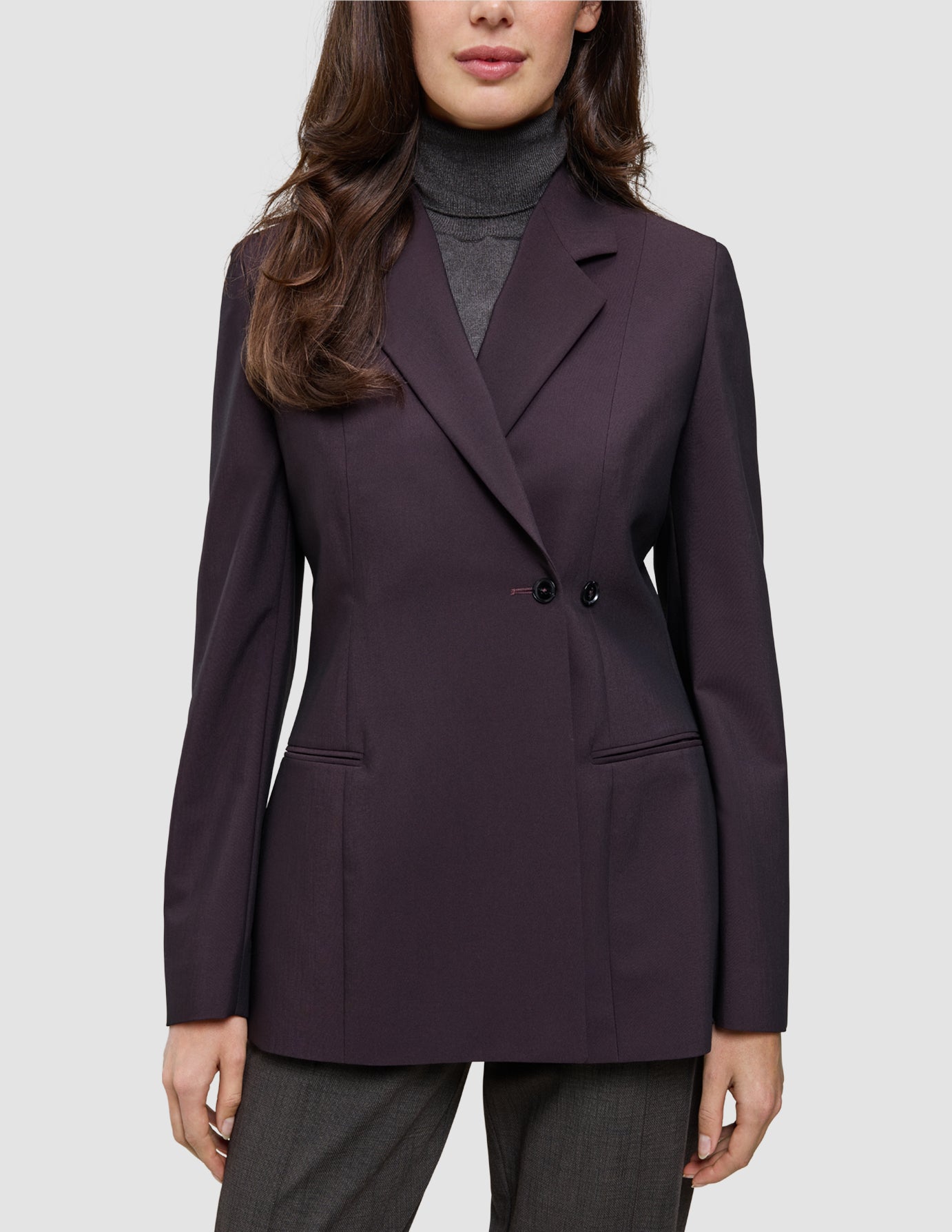 En person iført en Avira-blazer i farven Burgundy Berry til kvinder over en grå rullekravesweater, der afspejler klassisk dansk design.