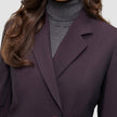 Et nærbillede af en person, der bærer en burgunderfarvet Women’s Avira Blazer Burgundy Berry over en grå rullekravesweater.