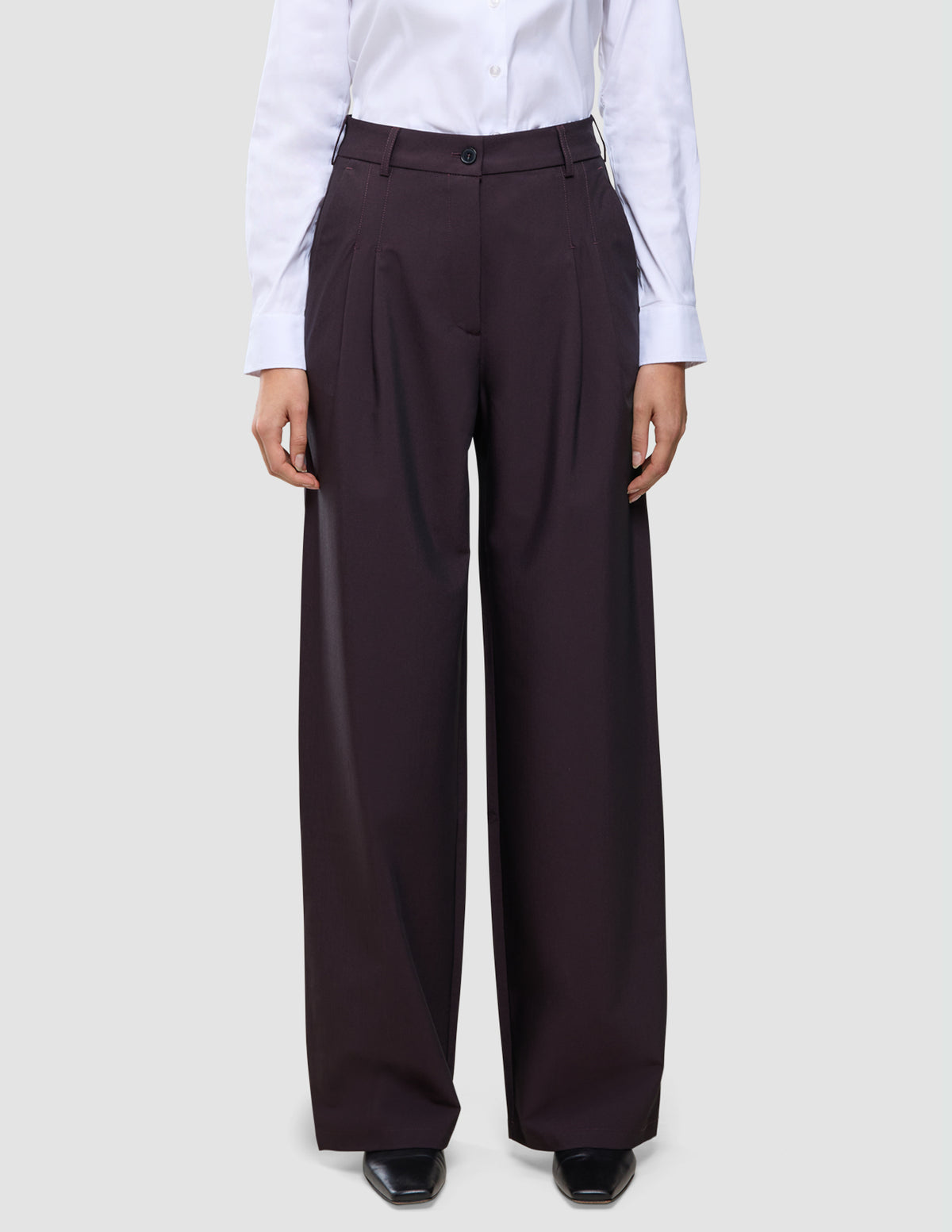En person iført en hvid skjorte med knapper, der er stoppet ned i et par mørkeburgunderfarvede Avira-bukser til kvinder med høj talje i modellen Wide Burgundy Berry.