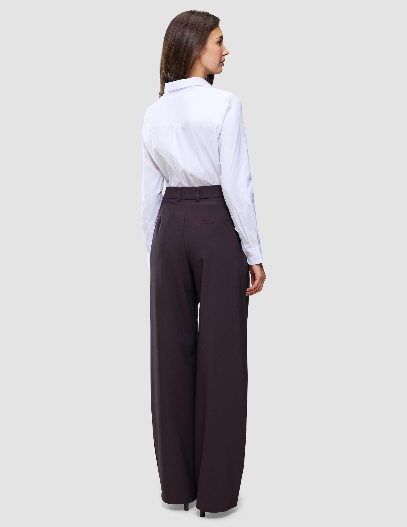 En kvinde set bagfra, iført en hvid skjorte med knapper, der er stukket ned i et par Avira-bukser til kvinder i modellen Wide i farven Burgundy Berry.