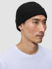 En person, der bærer en Beanie Black – en enkel, sort, ribstrikket hue i merinould i dansk stil.