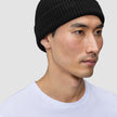 En person, der bærer en Beanie Black – en enkel, sort, ribstrikket hue i merinould i dansk stil.