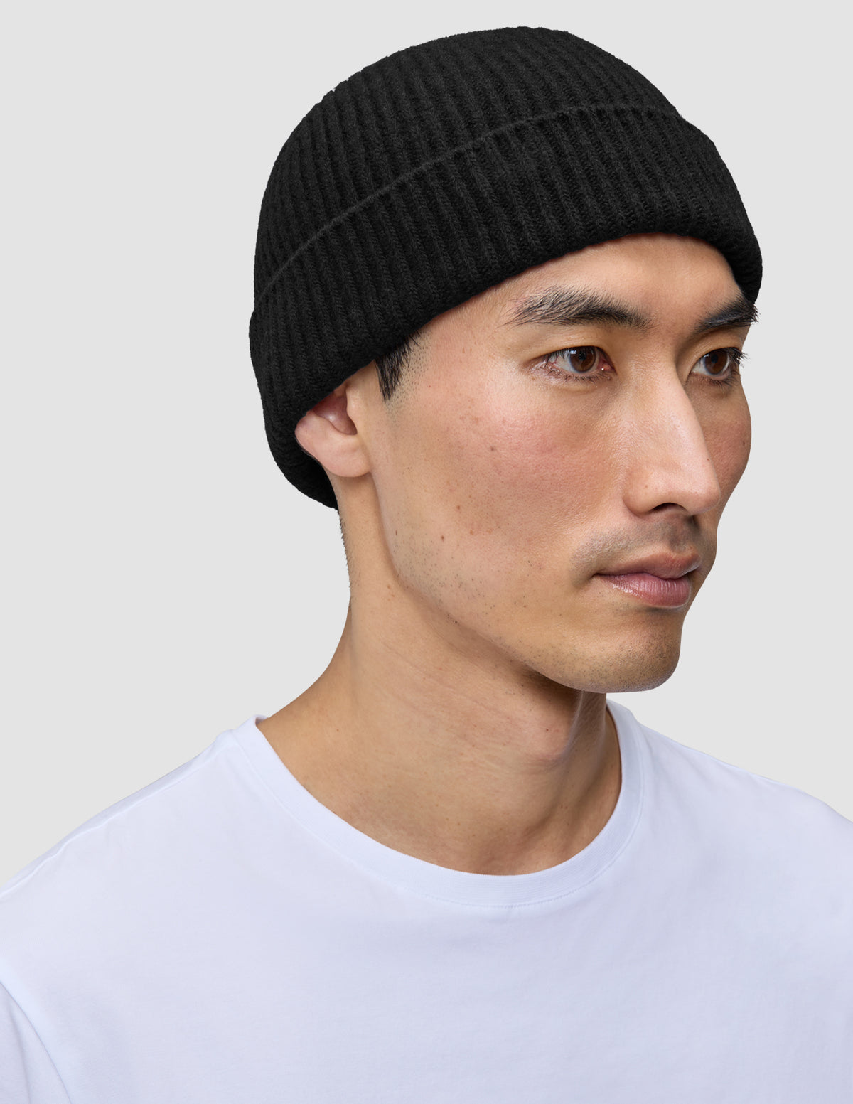 En person, der bærer en Beanie Black – en enkel, sort, ribstrikket hue i merinould i dansk stil.