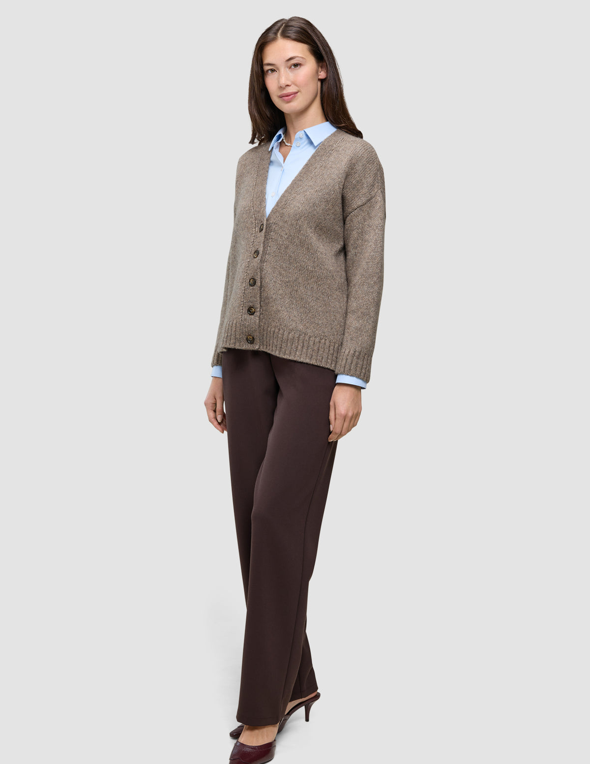En model iført en Chunky Soft Wool Knit Cardigan i farven Taupe Melange til kvinder over en lyseblå skjorte og brune bukser.