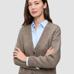 En kvinde iført en tyk, blød uldstrikket cardigan i farven taupe melange over en lyseblå skjorte med knapper.